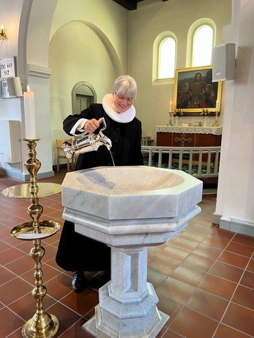 Præsten hælder vand i døbefonten